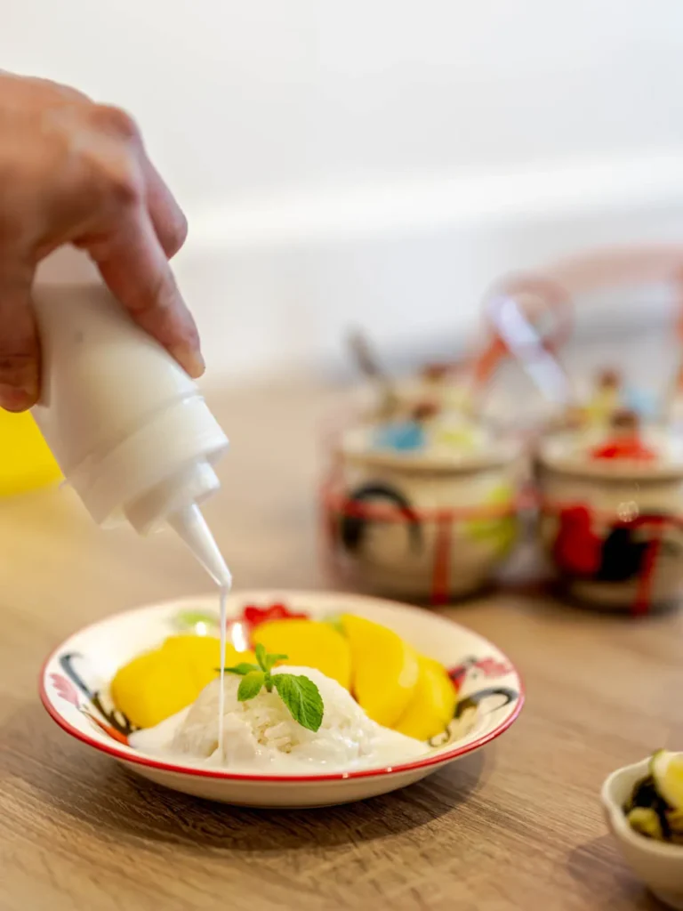 Fresh mango sticky rice being drizzled with creamy coconut sauce at Siam Bowl Amsterdam.